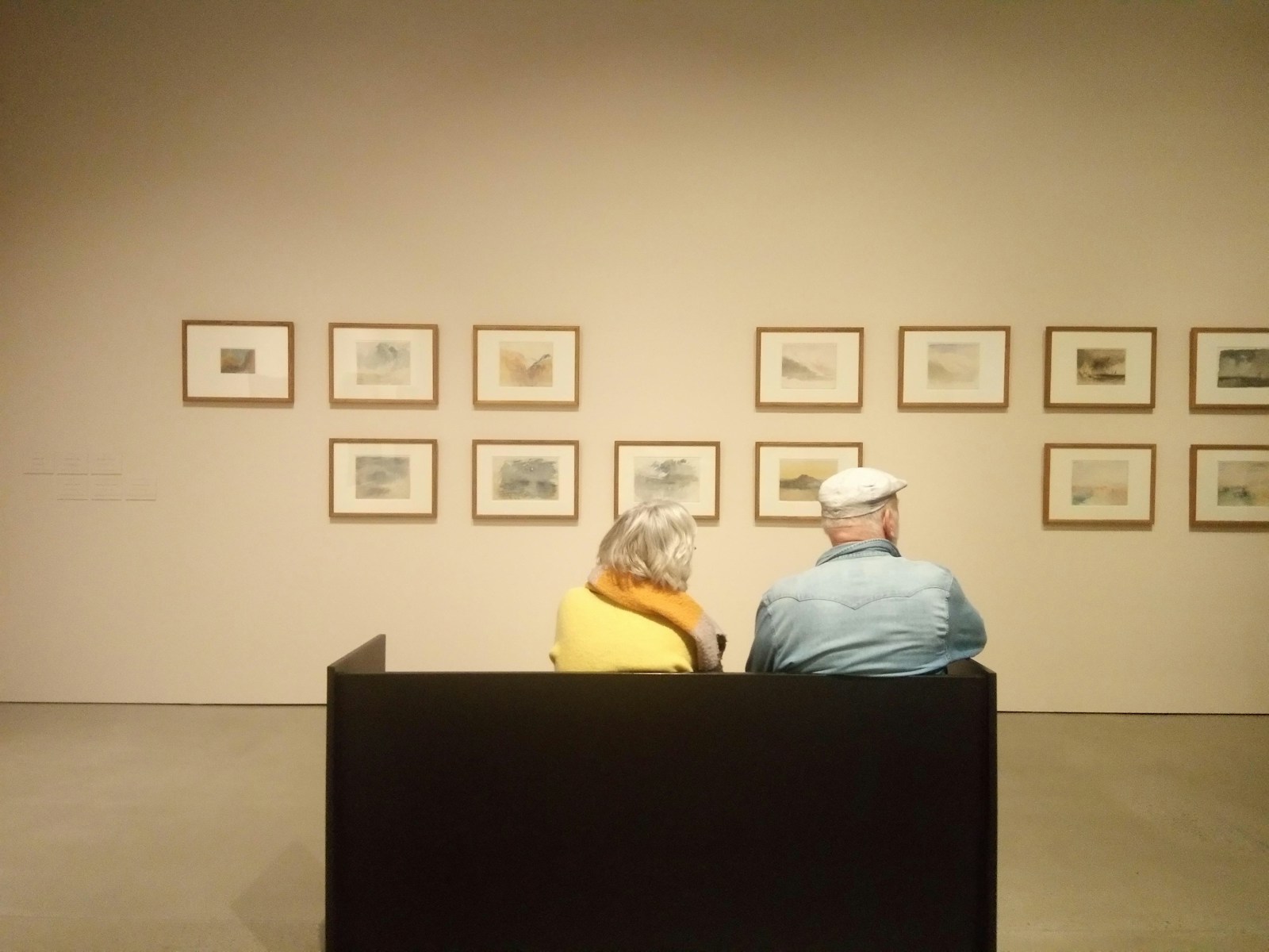 a man and a woman sitting on a bench in front of a wall with pictures