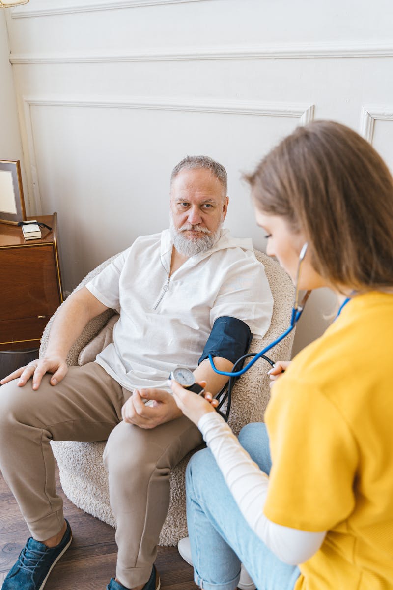 Photo by Antoni Shkraba Studio An elderly man having his blood pressure checked by a nurse during a routine health checkup indoors.
